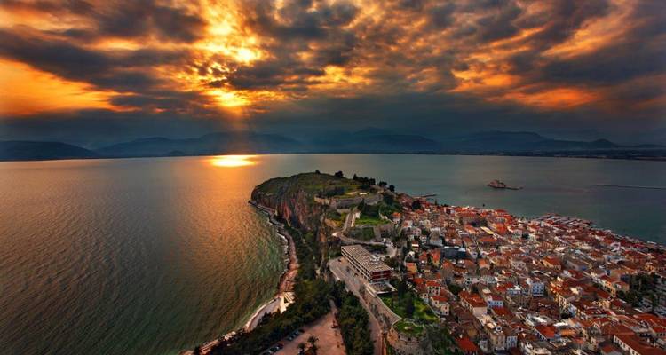 Dramatic sunset over Nafplio peninsula and Argolic Gulf, fiery rays piercing stormy clouds.