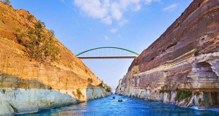 The steep-walled Corinth Canal with turquoise water spanned by a green arch bridge under bright sky.