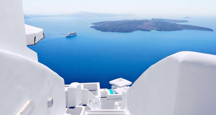 Pristine white Cycladic stairs descending toward the caldera of Santorini with a cruise ship on the blue Aegean Sea.