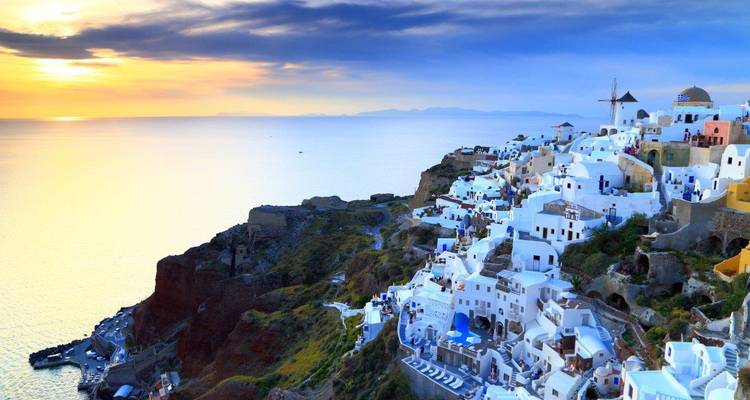 Iconic whitewashed village of Oia spilling down volcanic cliffs at sunset, overlooking calm Aegean waters.