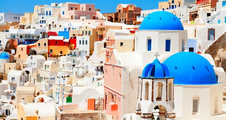 Close-up of blue-domed churches and pastel Cycladic houses under a bright sky in Oia, Santorini.