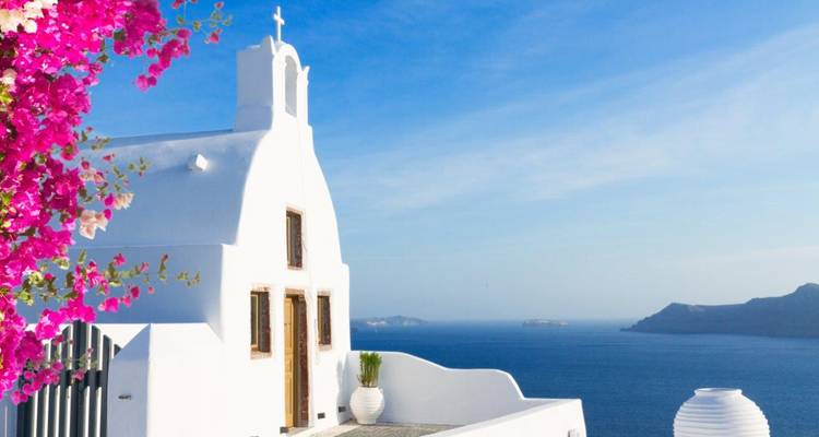 A small white chapel with cross and pink bougainvillea framing an expansive caldera view.
