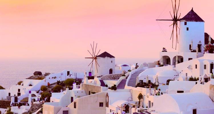 Soft pink sunset light over Oia’s terraced white houses and windmills overlooking the horizon.