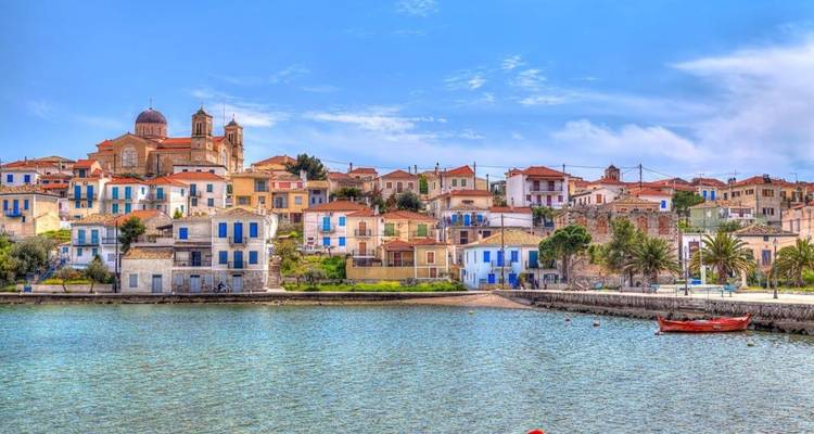 Colorful seaside village with a domed church and red-roofed houses lining a tranquil bay.