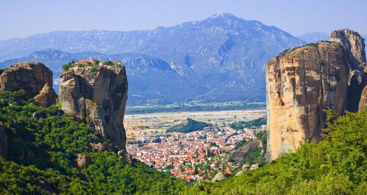 Wide valley view framed by two massive rock columns of Meteora with a town nestled below.