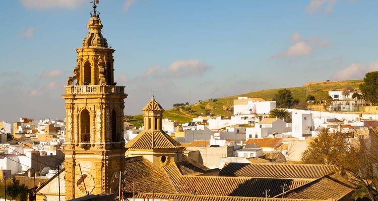 Bell tower of a historic church rising above whitewashed Andalusian rooftops under a blue sky.