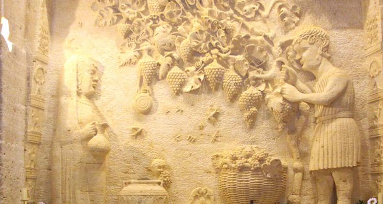 Carved stone relief inside a cave featuring figures harvesting grapes and decorative motifs.