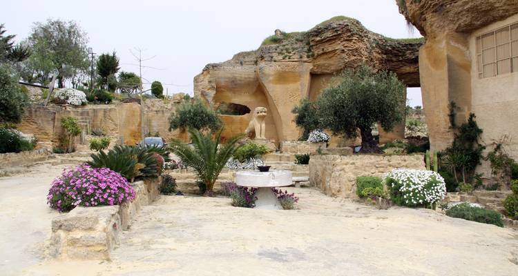 Open-air garden area of a sandstone quarry with flowers, palms and sculpted features.