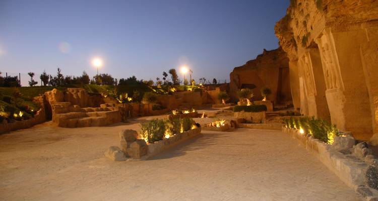 Nighttime view of an illuminated quarry courtyard with rock walls and landscaped paths.