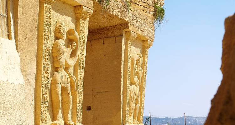 Sandstone pillars carved with human figures and decorative panels at an outdoor site.