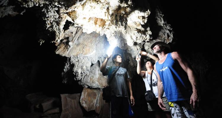 Three travellers illuminate dramatic cave formations with flashlights during an underground exploration.