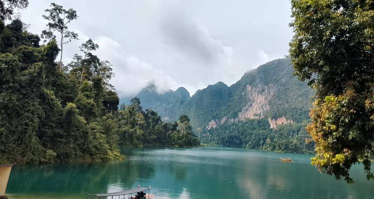 A tranquil turquoise lake is fringed by dense jungle and limestone mountains under a soft sky.