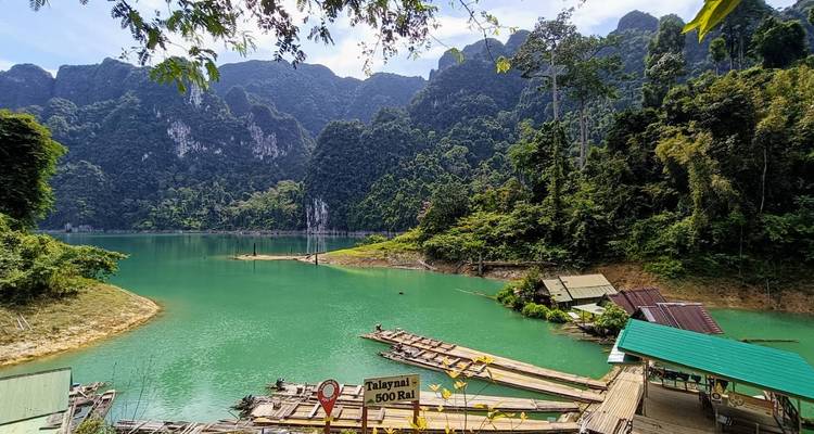 Bright green water fills a wide reservoir surrounded by towering limestone cliffs and floating wooden rafts.