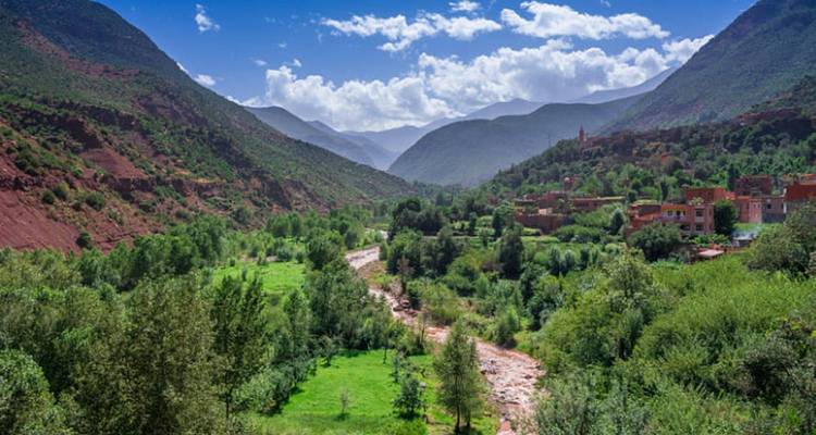 Lush Ourika Valley river winding between towering green Atlas peaks.