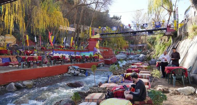 Colorful riverside café seats line both banks of a shallow stream.