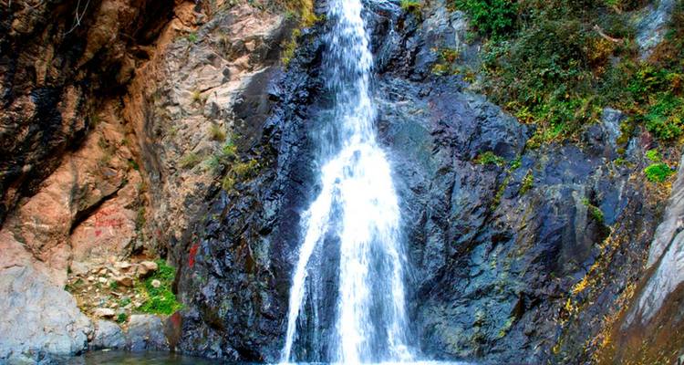 Slim waterfall cascades down dark rock face into a clear pool.