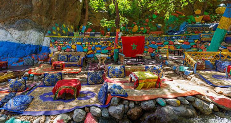 Vibrant cushions and carpets arranged beside a stream with Moroccan flag backdrop.