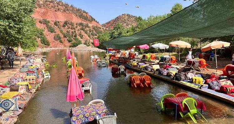 Shaded river dining area with umbrellas and patterned cushions in valley.