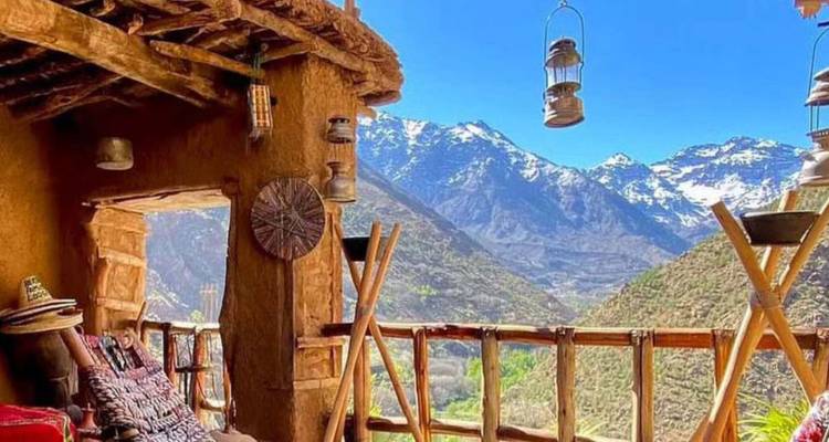A rustic terrace overlooks snowy Atlas peaks and a lush green valley.
