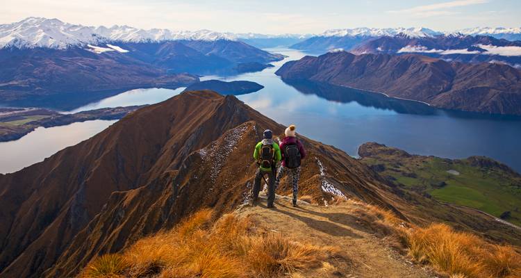 Dos excursionistas se encuentran en una cresta afilada con vista al Lago Wanaka y picos nevados