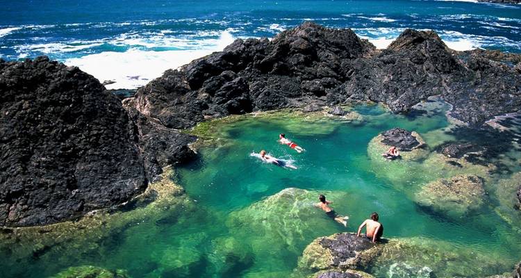 Los nadadores disfrutan de las piscinas naturales de roca turquesa junto al oleaje del océano