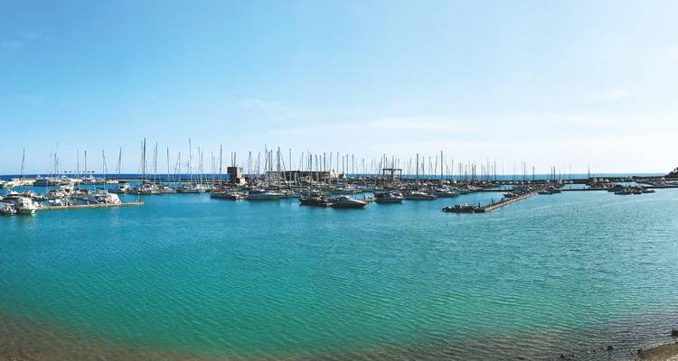 A panoramic marina filled with sailboats moored in the clear blue waters of Marina di Ragusa.