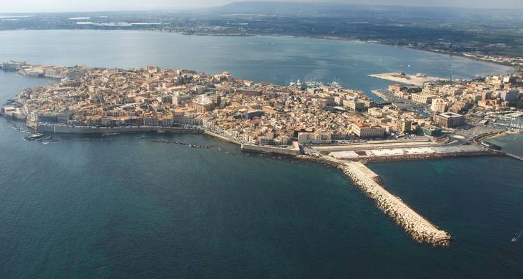 Aerial view of the island of Ortigia surrounded by the Ionian Sea and connected by a narrow causeway.