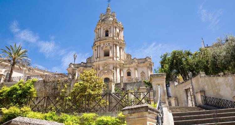 The ornate baroque Church of San Giorgio rises above cascading stone steps under a vivid blue sky.