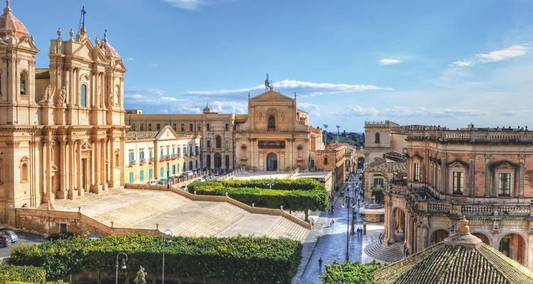 Sunlit baroque façades flank the grand square of Noto with sweeping views down a historic street.