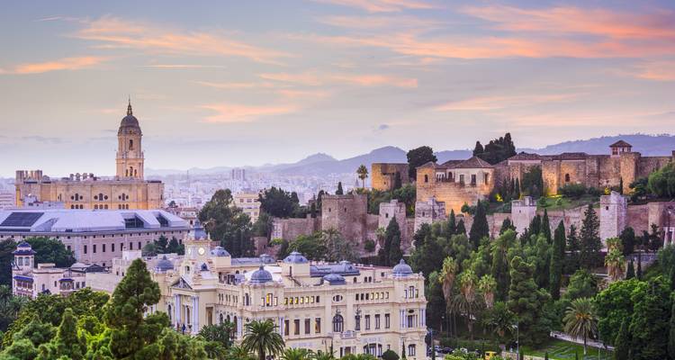 Soft dusk colours over Malaga showing the Alcazaba fortress, cathedral tower and lush city parklands.