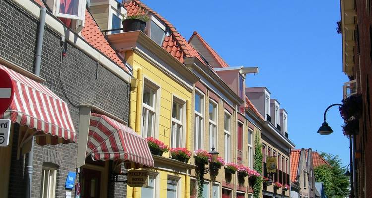 Charmante Nederlandse straat met kleurrijke puntgevels en gestreepte luifels onder een heldere blauwe hemel