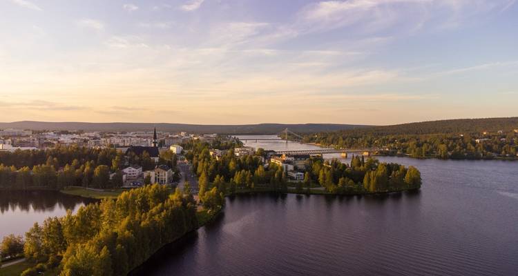 Aerial view of riverfront city with bridges, trees and calm water at sunset in Finnish Lapland