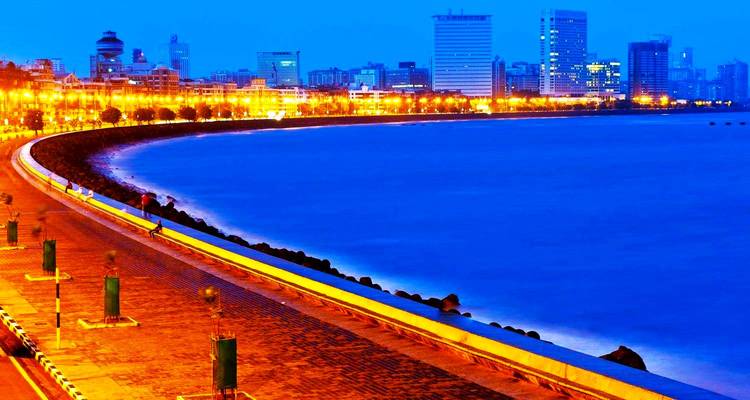 Illuminated Marine Drive arc and Mumbai skyline reflected in deep blue twilight.
