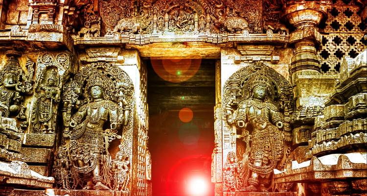 Elaborately carved temple doorway with dramatic lens flare illuminating stone deities.