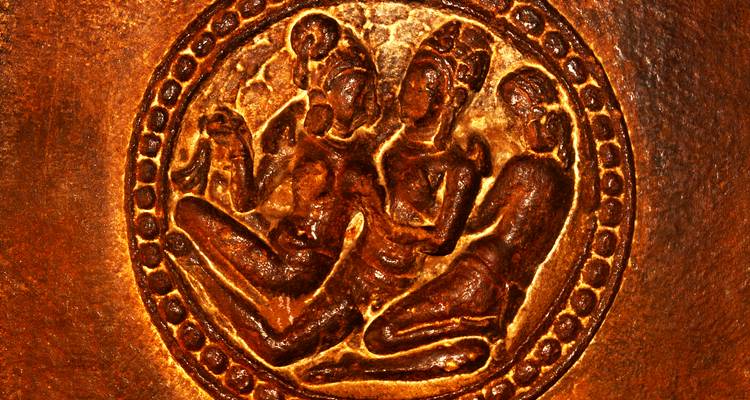 Close-up of ancient bronze relief depicting three seated figures.