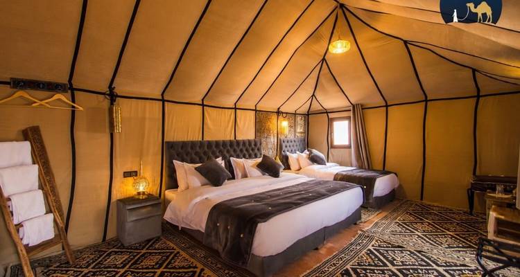Interior of a canvas tent with twin large beds, patterned carpet and warm lighting.