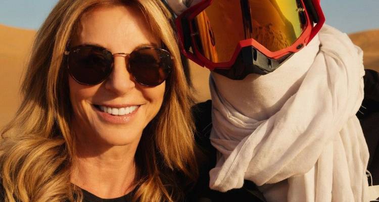 Smiling woman poses beside a masked ATV rider in desert sand dunes.