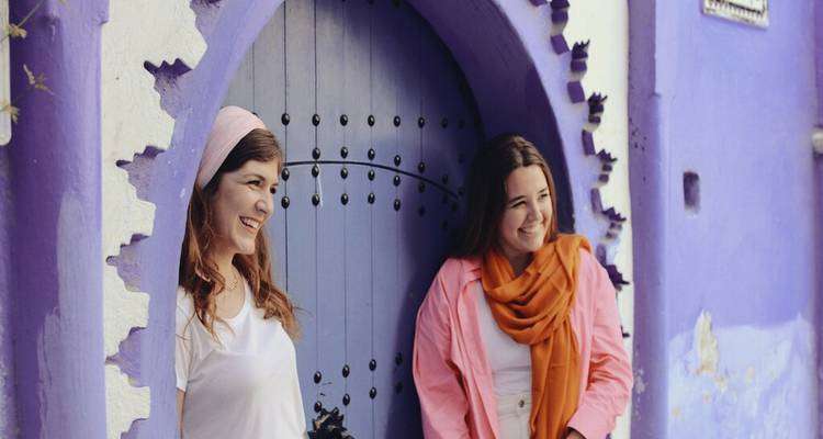 Two smiling women posing by a blue arched doorway in Chefchaouen