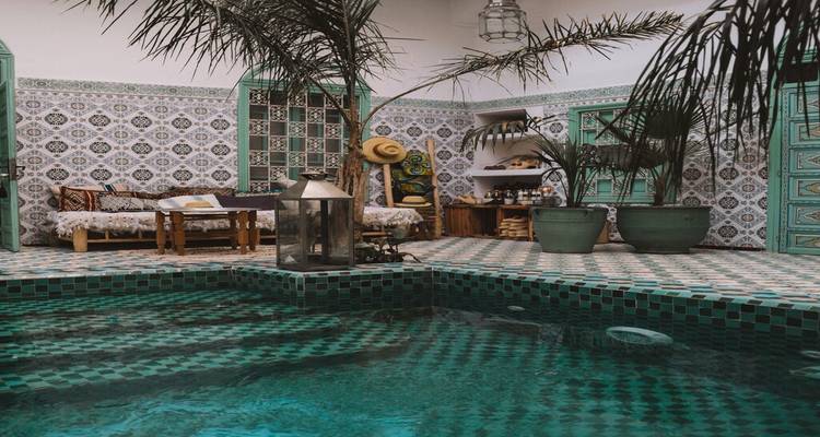Stylish riad courtyard with turquoise tiled pool, patterned walls and palms