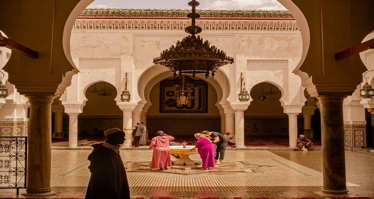 Visitors inside ornate courtyard of historic Moroccan mosque with grand chandelier