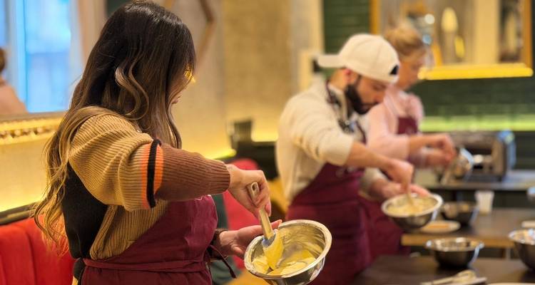 Participants in a cooking class mixing ingredients in metal bowls while wearing aprons.