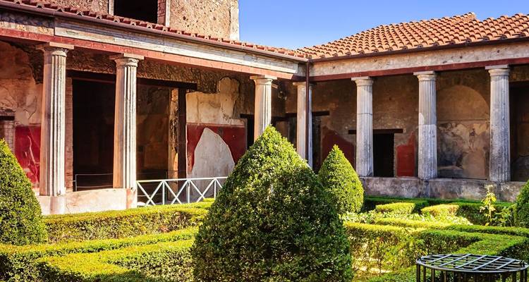 Restored Roman courtyard garden with manicured hedges and columned portico in Pompeii.