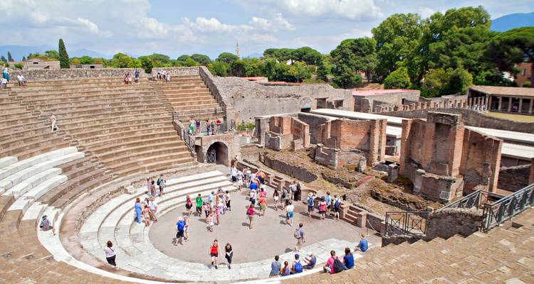 Crowds explore the ancient stone amphitheatre and ruins of Pompeii under a bright sky.