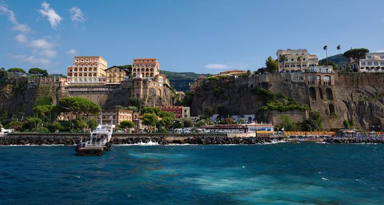 Clifftop town of Sorrento rises above deep blue sea and a bustling harbor under clear skies.