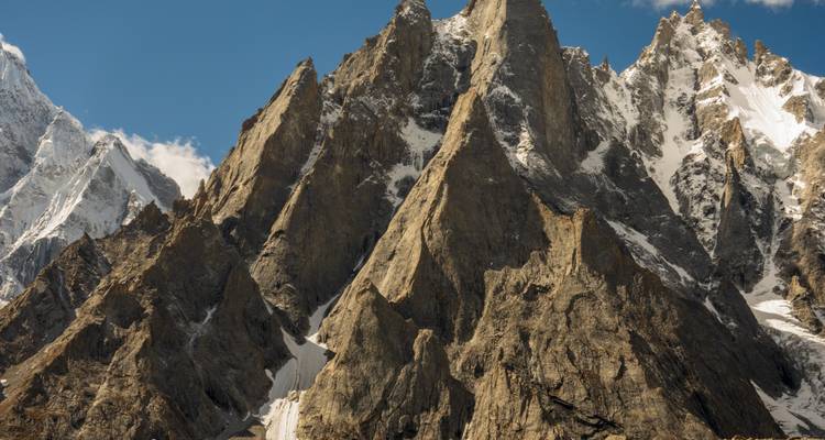 Close-up zicht op dramatische, gekartelde granieten bergspitsen bestoven met sneeuw onder helderblauwe luchten.