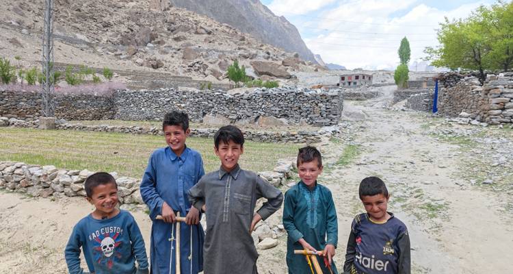 Vijf lokale kinderen glimlachen naar de camera terwijl ze handgemaakte speelgoed vasthouden in een bergdorp met stenen muren.