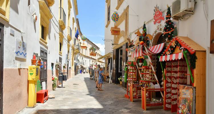 Calle italiana estrecha decorada con un puesto de mercado festivo que vende adornos, edificios coloridos y una pareja paseando.