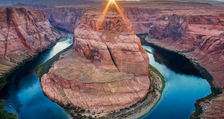 The Colorado River curves around the massive sandstone butte of Horseshoe Bend, lit by a dramatic sunburst.