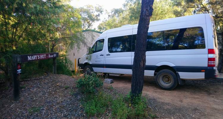 Tour van parked near a rustic forest hut marked 'Mary's Hut' on a dirt track.