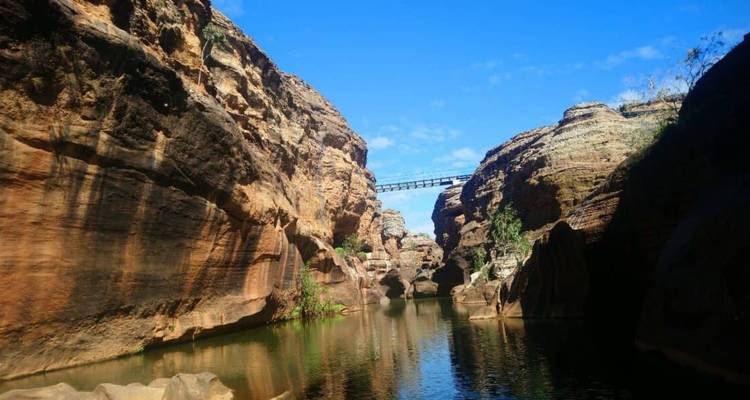 Gorge de grès profonde avec une eau verte et immobile et un étroit pont piétonnier situé bien au-dessus entre les parois rocheuses.